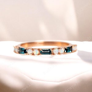 May include: A delicate gold band ring with alternating blue and white gemstones. The ring features small round white opals and rectangular blue gemstones.