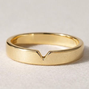 May include: A gold-colored ring with a flat band and a V-shaped notch. The ring has a smooth, matte finish and a simple, modern design. The ring is likely made of gold or a gold-colored metal.