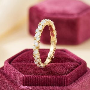 以下が含まれることがあります： 金色のリングで、マーキス型の虹色の宝石が並んでいます。リングは深紅のベルベットの背景に置かれ、石の輝きを際立たせています。ジュエリーです。