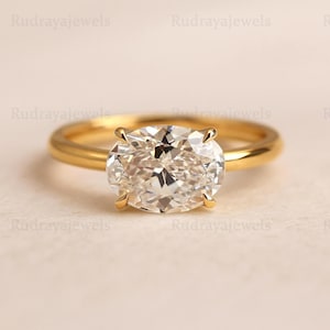 Op de afbeelding: Een gouden ring met een grote, ovaal geslepen diamant. De heldere, gefacetteerde diamant reflecteert het licht. De band is van eenvoudig, gepolijst goud. De ring is geplaatst tegen een neutrale achtergrond.