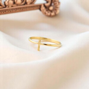 Pode incluir: Um anel dourado com um design de cruz simples. O anel &eacute; fino e delicado, e a cruz est&aacute; centralizada na banda.