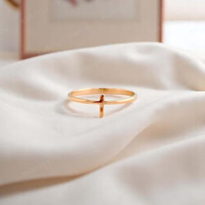 Pode incluir: Um anel dourado com um design simples de cruz. O anel &eacute; fino e delicado, e a cruz est&aacute; centralizada na banda.