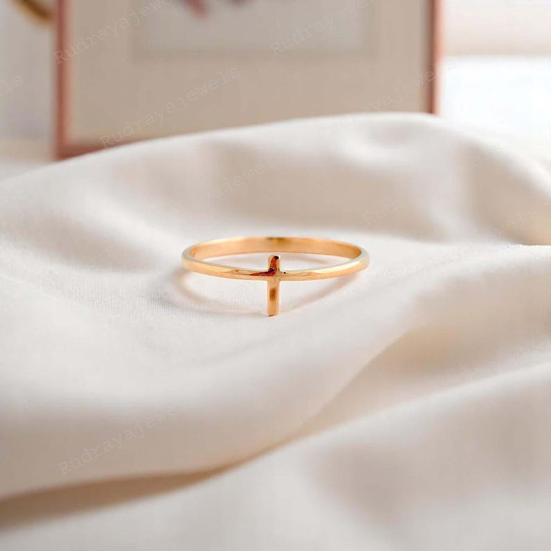 Pode incluir: Um anel dourado com um design simples de cruz. O anel &eacute; fino e delicado, e a cruz est&aacute; centralizada na banda.