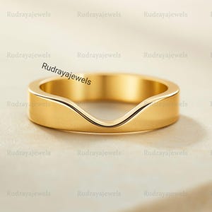 May include: A gold-colored ring with a curved design. The ring has a smooth, polished surface and a unique shape. The text "Rudrayajewels" is visible on the ring. This ring is a piece of jewelry.