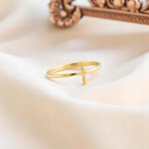 Pode incluir: Um anel dourado com um design de cruz simples. O anel &eacute; fino e delicado, e a cruz est&aacute; centralizada na banda.