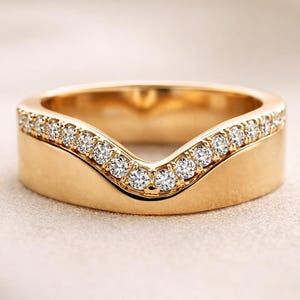 May include: A gold ring with a distinctive curved shape. The top of the ring is set with small, brilliant diamonds. The band is a smooth, polished gold, providing a contrast to the sparkling stones.
