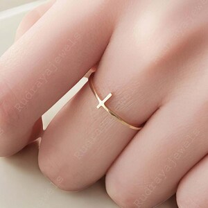 Pode incluir: Um delicado anel dourado com um design simples de cruz. O anel &eacute; fino e minimalista, perfeito para o uso di&aacute;rio.