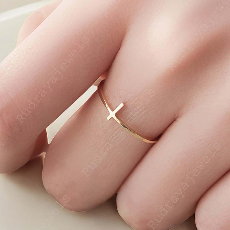 Pode incluir: Um delicado anel dourado com um design simples de cruz. O anel &eacute; fino e minimalista, perfeito para o uso di&aacute;rio.