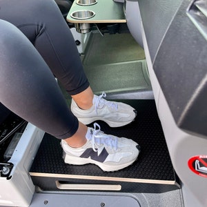 May include: A black and white honeycomb patterned floor mat with a wooden platform and a black cup holder with two stainless steel cups. The cup holder is mounted on a black surface.