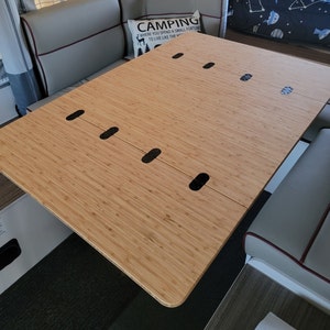May include: A light brown bamboo table top with black metal hinges. The table top is made of multiple panels that can be folded together. The table top is sitting on a white surface.