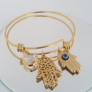 Puede incluir: Pulsera de oro con tres dijes: un cristal transparente, una mano de hamsa y una mano de hamsa con un ojo turco azul.