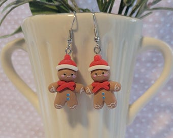 May include: A pair of gingerbread man earrings with red hats and white trim. The earrings are made of polymer clay and have silver hooks.