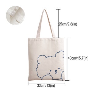 May include: A white canvas tote bag with a blue outline of a cartoon bear's head. The bag measures 15.7 inches tall, 13 inches wide, and 9.8 inches deep.