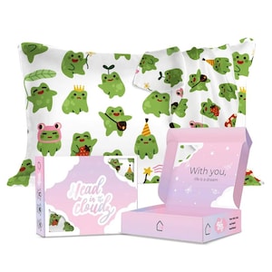 May include: A pink and white box with a frog design on the front. The box says "Head in the Clouds" and "With you, life is a dream". The box is open and there are two pillows inside. The pillows are white with a frog design on them.