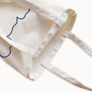 May include: A white canvas tote bag with a blue outline of a cloud on the front. The bag has two long straps.