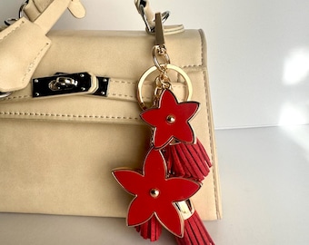 May include: A beige handbag with a gold chain and two red flower-shaped charms with tassels.