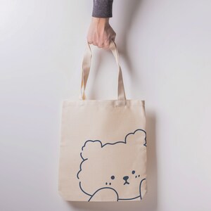 May include: A beige canvas tote bag with a simple line drawing of a bear's face on the front.