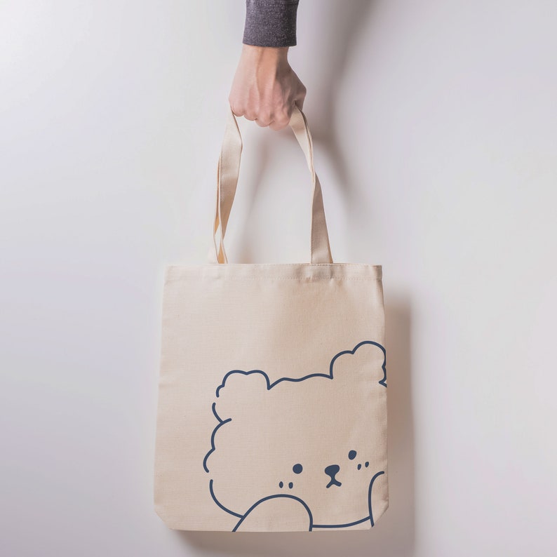 May include: A beige canvas tote bag with a simple line drawing of a bear's face on the front.
