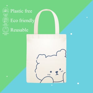 May include: White tote bag with a blue outline of a cartoon bear's face. The bag has the text "Plastic free", "Eco friendly", and "Reusable" printed on it.