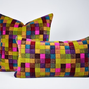 Pode incluir: Duas almofadas decorativas com um padrão geométrico vibrante. As almofadas apresentam um design de patchwork de quadrados coloridos em tons de verde, rosa, roxo, azul e castanho. Uma almofada é quadrada e a outra retangular.