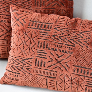 Puede incluir: Dos cojines decorativos con un patrón geométrico en tonos naranja y marrón. Los cojines están hechos de una tela suave y texturizada.