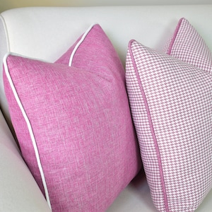 Könnte beinhalten: Zwei rosa Kissen mit weißen Paspeln. Ein Kissen hat einen einfarbigen rosa Stoff und das andere ein rosa-weißes Hahnentrittmuster.