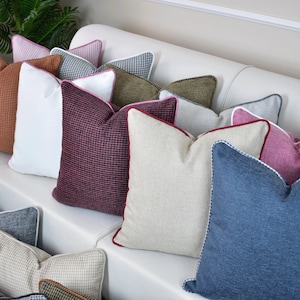 May include: A collection of decorative throw pillows in various colors and patterns, including brown, white, pink, red, beige, blue, and green. The pillows are arranged on a white couch.