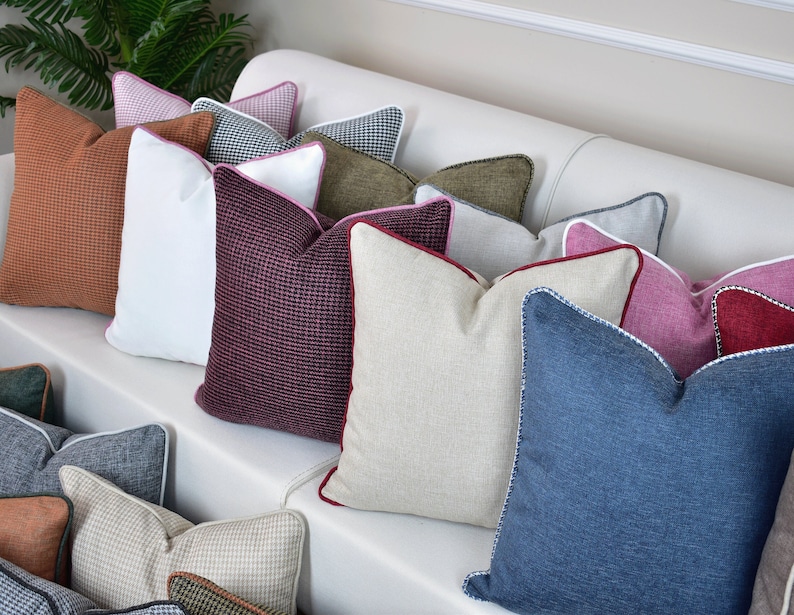 May include: A collection of decorative throw pillows in various colors and patterns, including brown, white, pink, red, beige, blue, and green. The pillows are arranged on a white couch.
