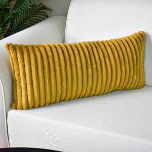 May include: A long, rectangular, mustard yellow pillow with a ribbed texture. The pillow is made of a soft, plush fabric.