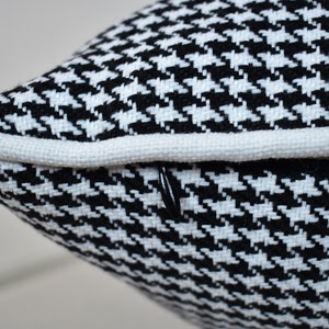 May include: Close-up of a black and white houndstooth pillow with a white piping around the edge.