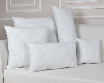 May include: Five white pillow inserts of various sizes are arranged on a white couch. The pillows are made of a soft, fluffy material and are perfect for adding comfort and support to any bed or sofa.