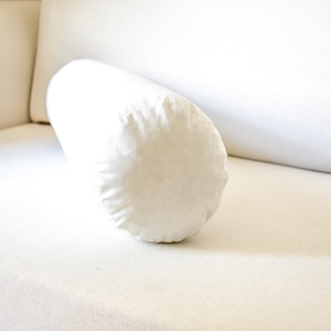 May include: A white cylindrical pillow resting on a white couch.