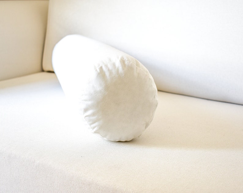May include: A white cylindrical pillow resting on a white couch.