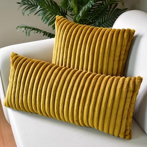 May include: Two mustard yellow corduroy throw pillows with a ribbed texture. The pillows are on a white couch.
