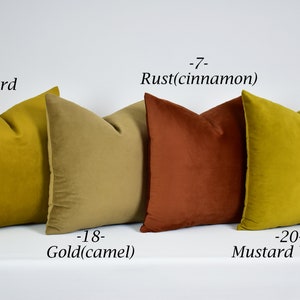 May include: Four decorative throw pillows in various shades of yellow, gold, and rust. The pillows are arranged in a row on a white surface. The pillows are labeled with their colors: Mustard, Rust (cinnamon), Gold (camel), and Mustard Yellow.