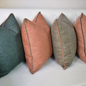 May include: Four decorative throw pillows in various patterns and colors. One is teal, two are coral with a small check pattern, and one is a black and tan houndstooth pattern. All pillows have a contrasting trim.