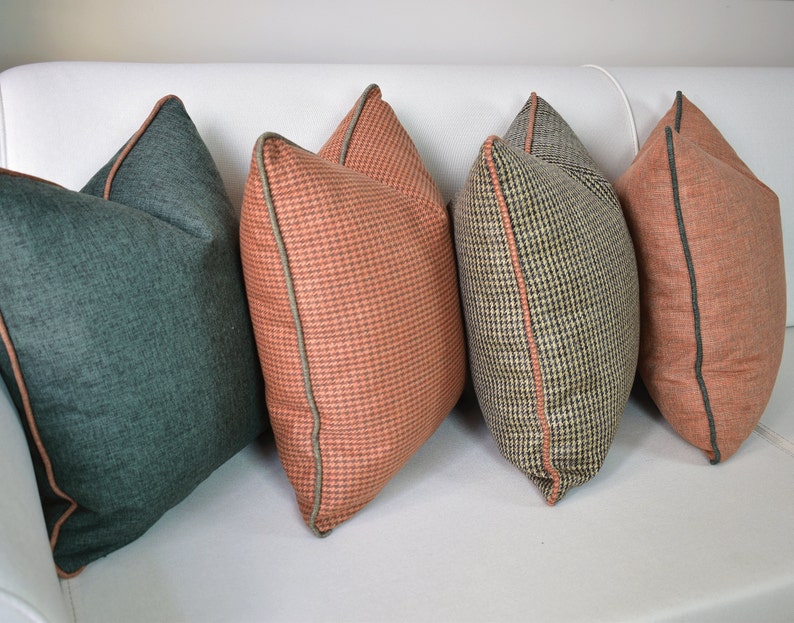 May include: Four decorative throw pillows in various patterns and colors. One is teal, two are coral with a small check pattern, and one is a black and tan houndstooth pattern. All pillows have a contrasting trim.