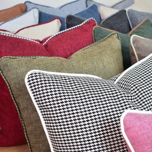 May include: A collection of decorative throw pillows in various colors and patterns. Pillows include red, green, black and white houndstooth, and pink. Each pillow has a contrasting border and a white or black trim.