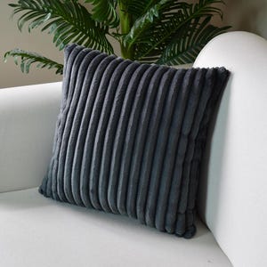 Könnte beinhalten: Ein dunkelgraues Kissen aus Cord mit weicher, plüschiger Textur. Das Kissen liegt auf einem weißen Sofa.