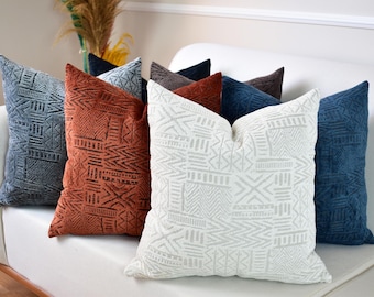 May include: A set of decorative throw pillows with geometric patterns in various colors, including white, gray, blue, and orange. The pillows are arranged on a white couch.