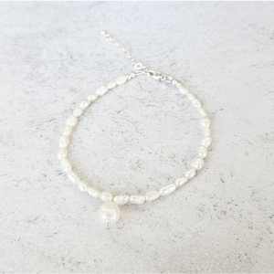 May include: A delicate white pearl necklace with a single, larger pearl pendant. The necklace is made of small, oval-shaped pearls strung together with a silver chain and clasp. The pendant hangs gracefully below the necklace's center.