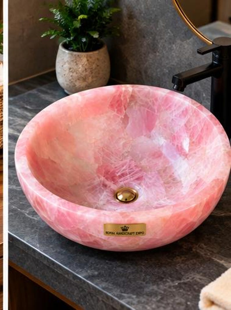 Pode incluir: Uma cuba de apoio redonda feita de pedra de quartzo rosa transl&uacute;cido com acabamento polido. A bacia apresenta um ralo dourado e uma pequena placa retangular dourada na frente com o texto Royal Handicraft Expo.