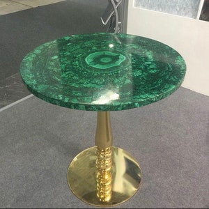 May include: A round green malachite table top with a gold metal base. The table top has a swirling pattern and a darker green center.