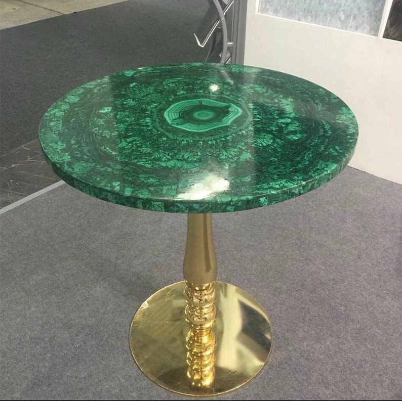 May include: A round green malachite table top with a gold metal base. The table top has a swirling pattern and a darker green center.