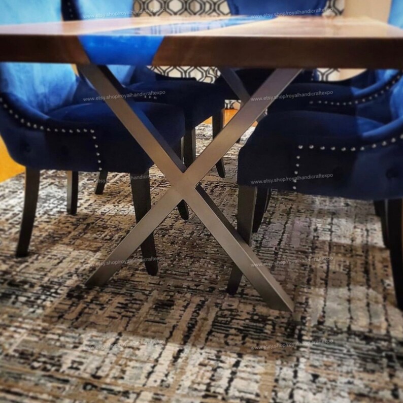 May include: A dark wood dining table with a blue epoxy resin inlay and a metal X-shaped base. The table is set with four blue velvet chairs.