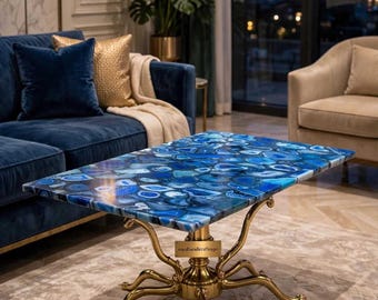 May include: A rectangular coffee table featuring a polished blue agate stone tabletop with varied shades of blue and white patterns. The table is supported by a gold-toned metal base with four curved legs and a small rectangular brand tag.