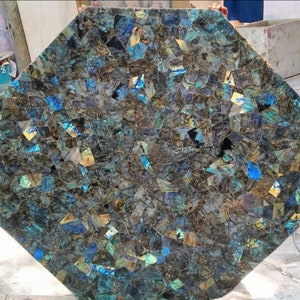 May include: Octagonal table top made of iridescent labradorite stone. The table top is made of many small pieces of labradorite, creating a mosaic effect. The labradorite is a dark blue and green color with iridescent flashes of gold and purple.