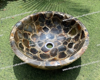 May include: A round, brown agate sink with a drain hole in the center. The sink is made of many small pieces of agate that have been polished and glued together. The sink is sitting on a bed of green grass.
