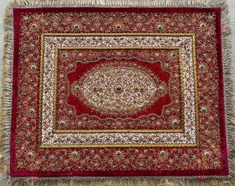 Puede incluir: Un tapiz de pared de terciopelo rojo bordado con acentos dorados y de color joya. El diseño presenta intrincados patrones florales y un motivo oval central.