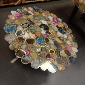 May include: A round table top made of agate slices in various colors, including brown, white, blue, green, and pink. The slices are arranged in a circular pattern and are held together by a metal frame. The table top is approximately 30 inches in diameter.